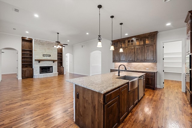 kitchen featuring sink, crown molding, a kitchen island with sink, a stone fireplace, and decorative light fixtures