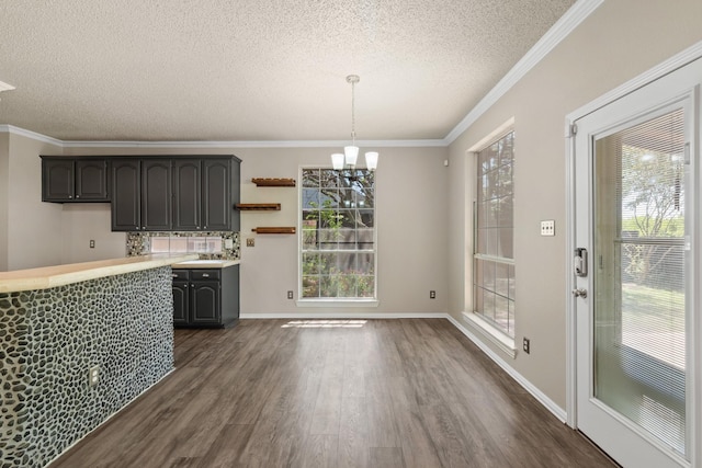 unfurnished dining area featuring an inviting chandelier, ornamental molding, a textured ceiling, and dark wood-type flooring