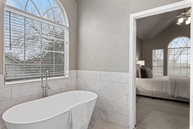 ensuite bathroom featuring tile walls, ceiling fan, a wealth of natural light, and connected bathroom