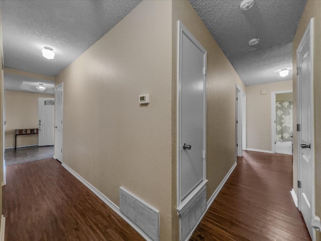 corridor with dark hardwood / wood-style floors and a textured ceiling