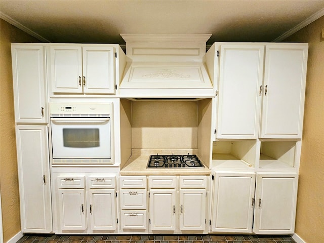 kitchen featuring premium range hood, stainless steel gas stovetop, oven, and white cabinets