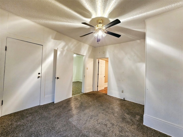 unfurnished bedroom featuring ceiling fan, dark carpet, and a textured ceiling