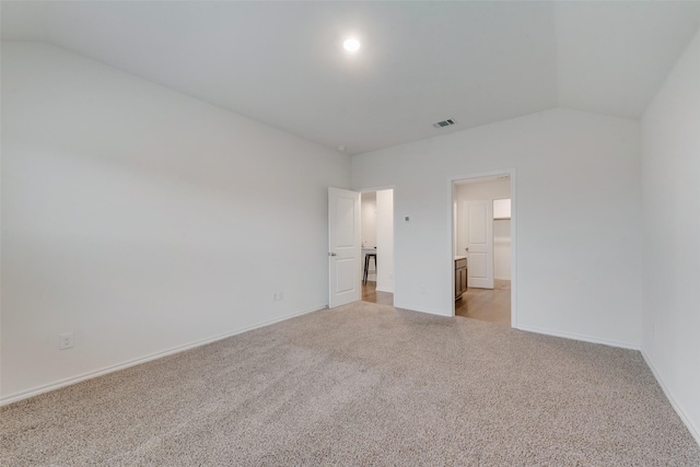 unfurnished bedroom featuring ensuite bath, vaulted ceiling, and light colored carpet