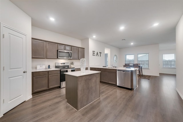 kitchen with appliances with stainless steel finishes, a kitchen island with sink, sink, and dark hardwood / wood-style flooring