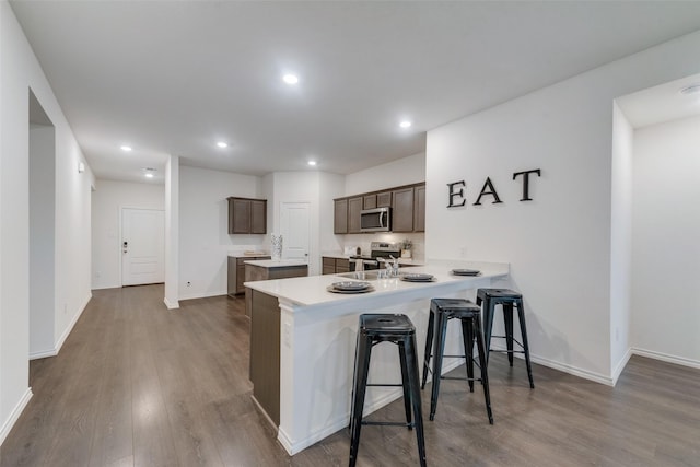 kitchen with wood-type flooring, a kitchen breakfast bar, kitchen peninsula, and appliances with stainless steel finishes