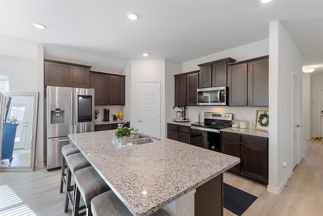 kitchen with a kitchen bar, a center island with sink, stainless steel appliances, light stone countertops, and light hardwood / wood-style floors