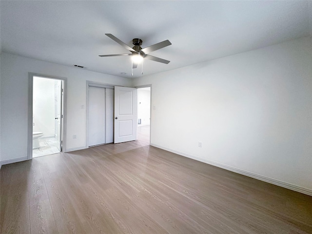 unfurnished bedroom featuring ensuite bathroom, ceiling fan, light hardwood / wood-style floors, and a closet