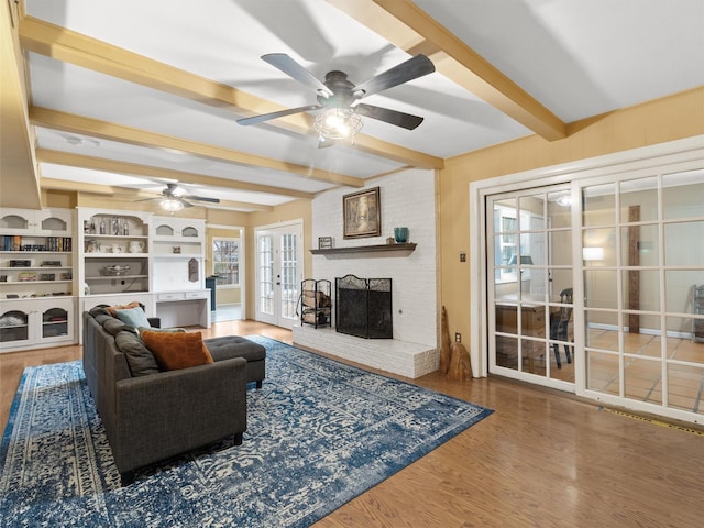 living room featuring ceiling fan, hardwood / wood-style floors, a brick fireplace, french doors, and beamed ceiling