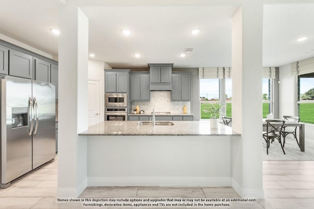 kitchen with gray cabinets, sink, backsplash, stainless steel appliances, and light stone countertops