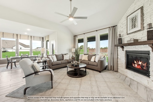 living room featuring ceiling fan, lofted ceiling, a stone fireplace, and a wealth of natural light