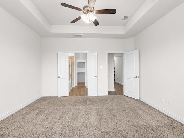 unfurnished bedroom with ceiling fan, a spacious closet, a raised ceiling, and carpet floors