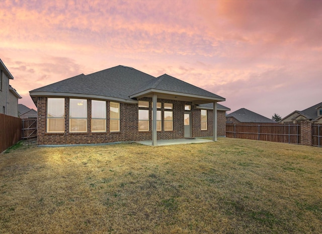 back house at dusk featuring a yard and a patio