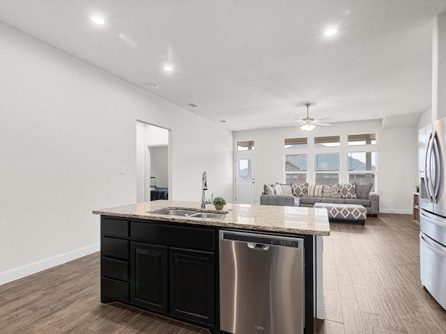 kitchen featuring sink, light stone counters, appliances with stainless steel finishes, dark hardwood / wood-style flooring, and a kitchen island with sink