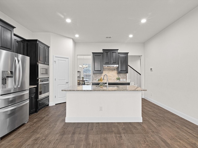 kitchen with sink, decorative backsplash, a kitchen island with sink, light stone counters, and stainless steel appliances