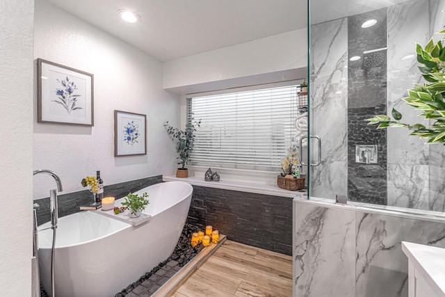 bathroom with wood finished floors, a marble finish shower, a soaking tub, recessed lighting, and a textured wall