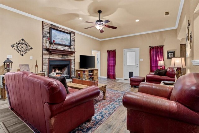 living area with a stone fireplace, wood finished floors, ceiling fan, and ornamental molding