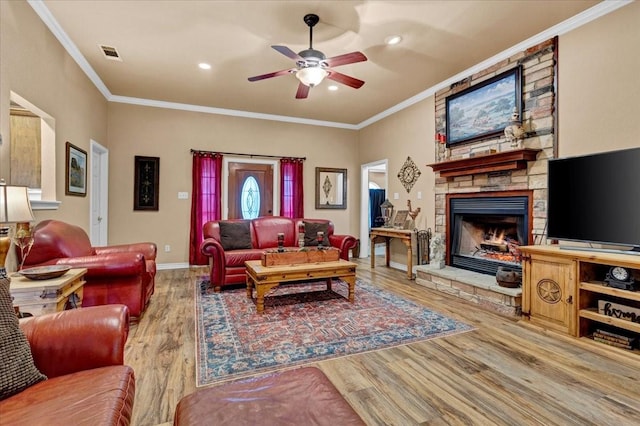 living room featuring crown molding, visible vents, a ceiling fan, a stone fireplace, and wood finished floors