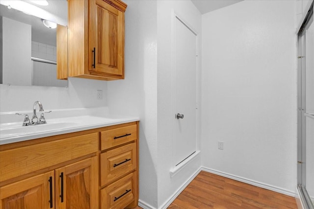full bath featuring a shower with door, baseboards, wood finished floors, and vanity