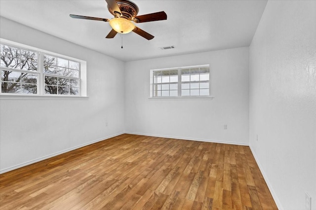 empty room with baseboards, visible vents, ceiling fan, and hardwood / wood-style flooring