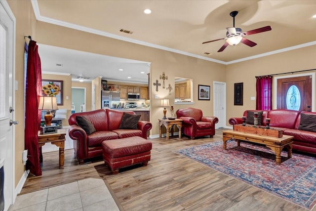 living room with visible vents, light wood-style floors, ornamental molding, and a ceiling fan