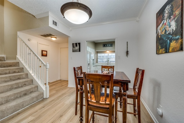 dining area with ornamental molding, sink, light hardwood / wood-style floors, and a textured ceiling