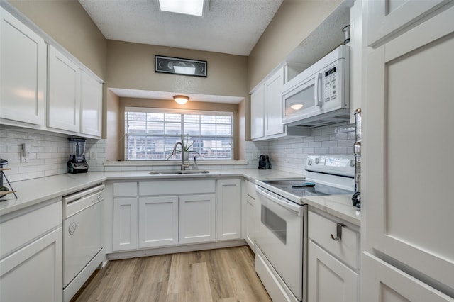 kitchen with white appliances, sink, white cabinetry, light hardwood / wood-style floors, and decorative backsplash