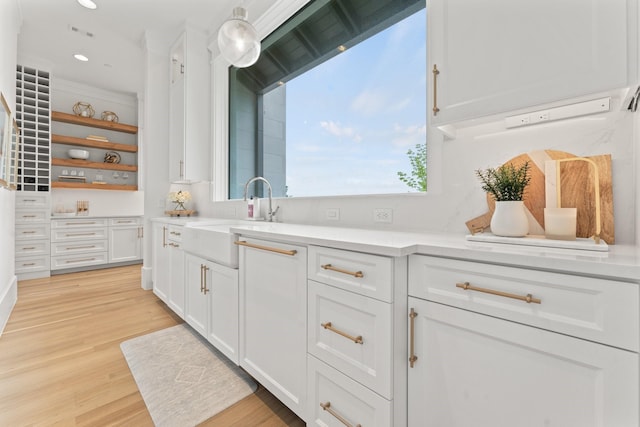 kitchen featuring white cabinetry, sink, pendant lighting, and light wood-type flooring