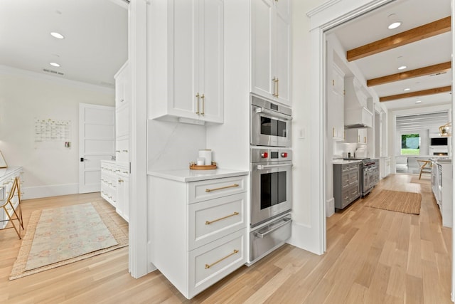 kitchen with premium range hood, white cabinets, light hardwood / wood-style floors, stainless steel appliances, and beam ceiling