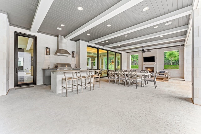 kitchen with wall chimney exhaust hood, gray cabinetry, a large fireplace, ceiling fan, and beam ceiling