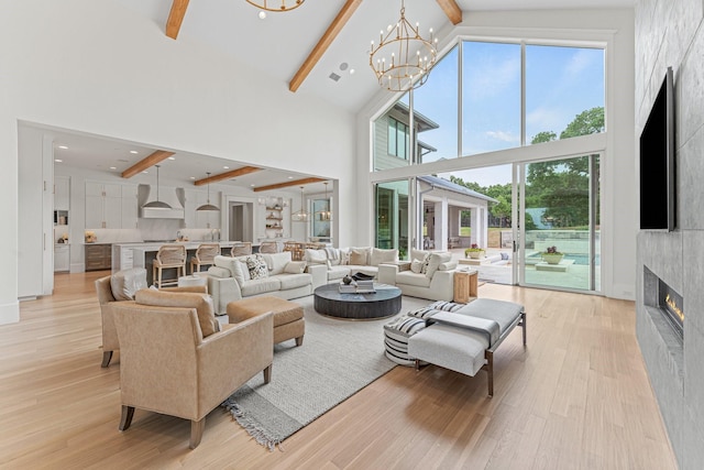 living room with high vaulted ceiling, beamed ceiling, a large fireplace, a notable chandelier, and light hardwood / wood-style floors