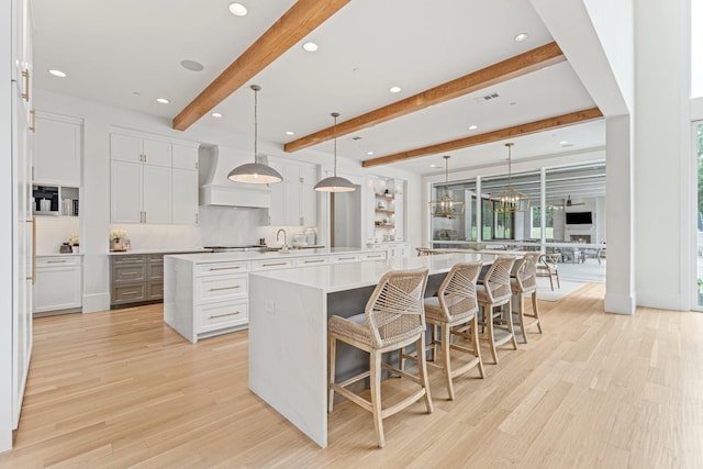 kitchen with custom exhaust hood, white cabinetry, hanging light fixtures, light hardwood / wood-style flooring, and a large island