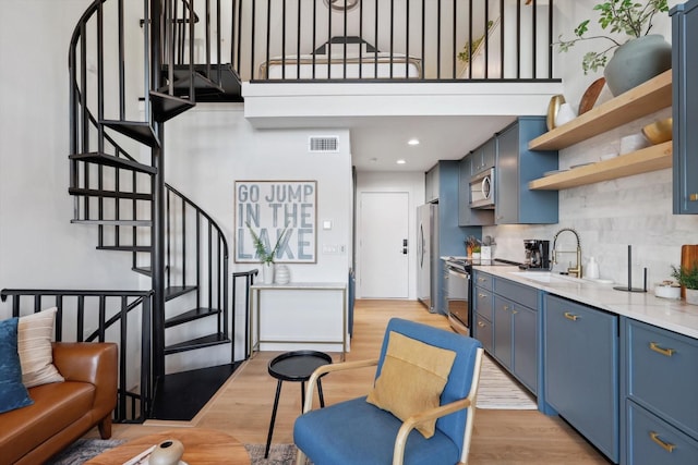 kitchen with appliances with stainless steel finishes, blue cabinets, sink, and light wood-type flooring