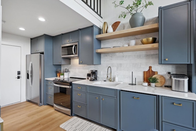 kitchen featuring blue cabinetry, sink, light wood-type flooring, stainless steel appliances, and decorative backsplash