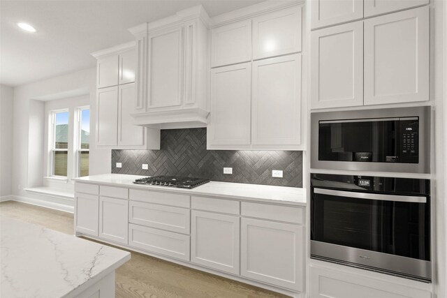 kitchen featuring stainless steel appliances, white cabinetry, light stone counters, and tasteful backsplash