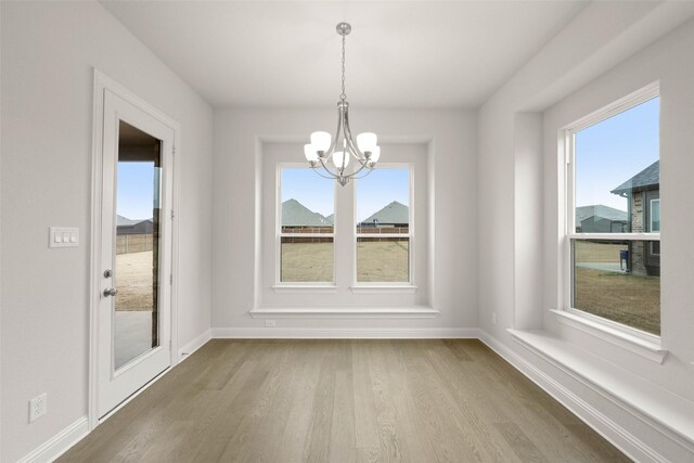 unfurnished dining area featuring an inviting chandelier, wood finished floors, and baseboards