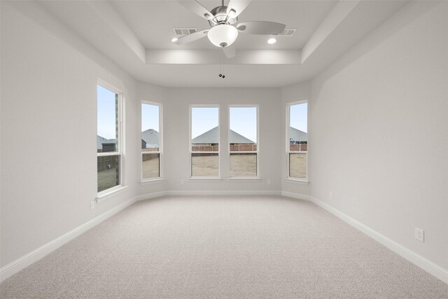 carpeted spare room featuring visible vents, a tray ceiling, a ceiling fan, and baseboards