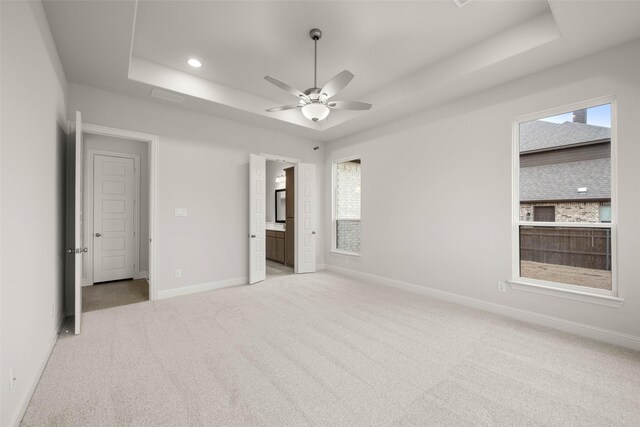 unfurnished bedroom with baseboards, a raised ceiling, light colored carpet, ensuite bath, and recessed lighting