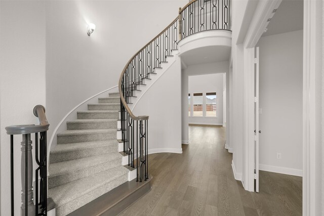 stairway with arched walkways, a towering ceiling, baseboards, and wood finished floors