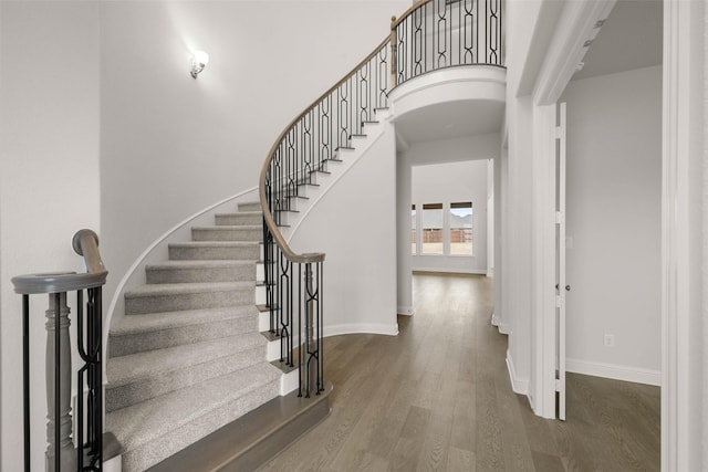 stairs with arched walkways, a towering ceiling, baseboards, and wood finished floors