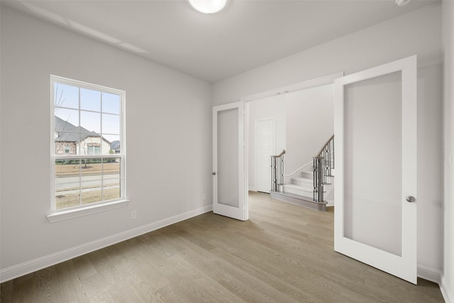 unfurnished room with light wood-style floors, stairway, and baseboards