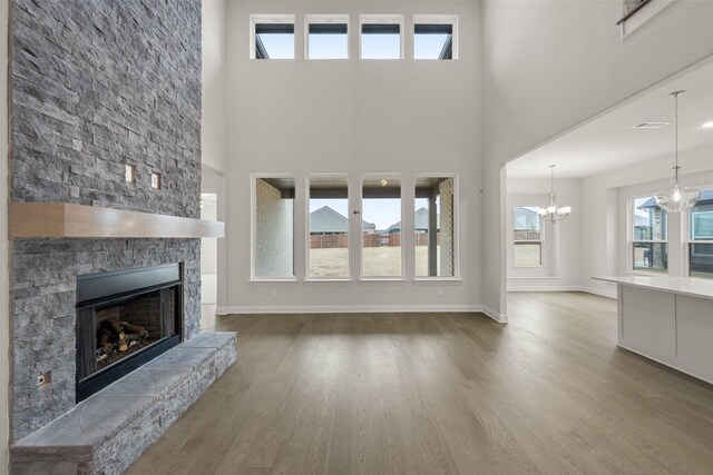 unfurnished living room with baseboards, a stone fireplace, wood finished floors, and a notable chandelier