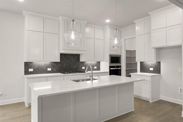 kitchen with an island with sink, light stone countertops, white cabinets, and hanging light fixtures