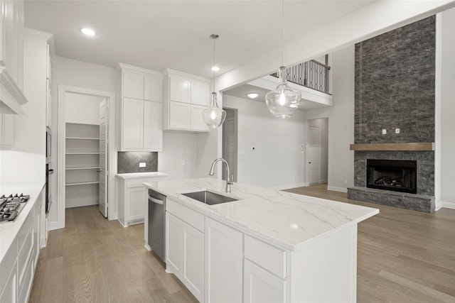 kitchen featuring white cabinets, a center island with sink, a sink, and light stone countertops
