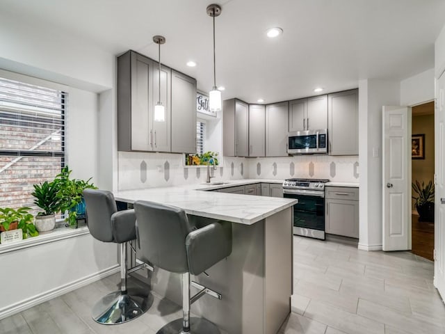 kitchen with sink, appliances with stainless steel finishes, gray cabinetry, decorative light fixtures, and kitchen peninsula