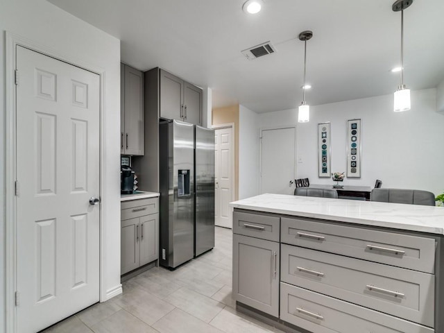 kitchen featuring stainless steel refrigerator with ice dispenser, pendant lighting, gray cabinetry, and light stone counters