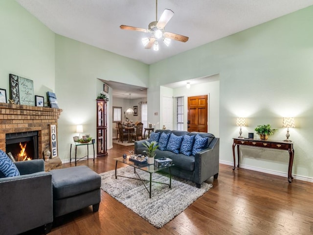 living room with dark wood-type flooring, ceiling fan, and a brick fireplace