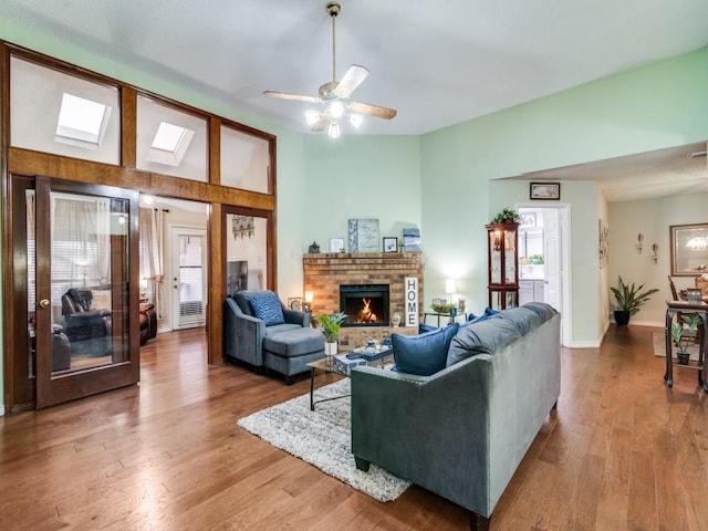 living room featuring lofted ceiling, hardwood / wood-style floors, ceiling fan, and a brick fireplace