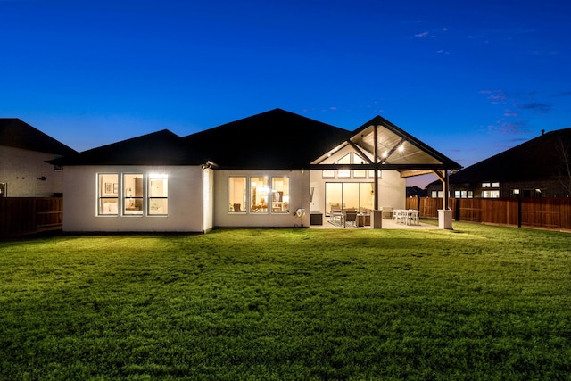 back house at dusk featuring a lawn and a patio