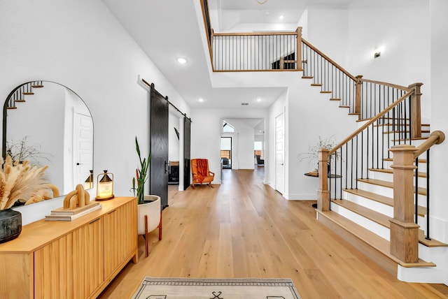 foyer entrance with a high ceiling, a barn door, and light hardwood / wood-style flooring