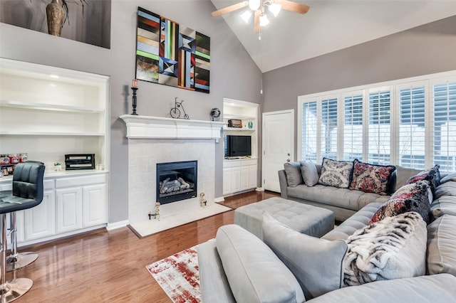 living room with built in shelves, high vaulted ceiling, hardwood / wood-style flooring, ceiling fan, and a fireplace